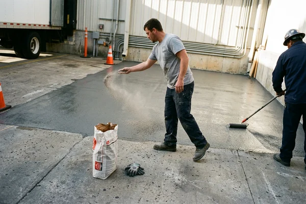 Crew broadcasting anti-slip aggregate onto a wet basecoat at a dock apron