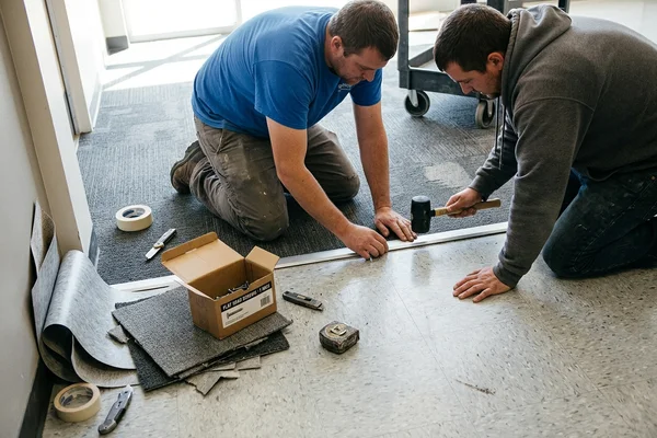 Crew setting a transition strip between carpet tile and sheet vinyl