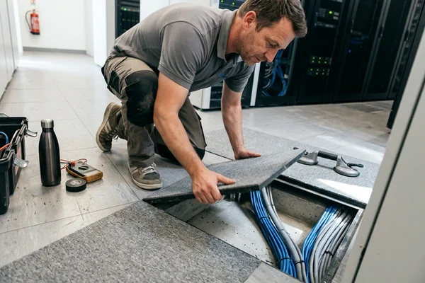 Installer lifting a single carpet tile beside a raised access floor panel