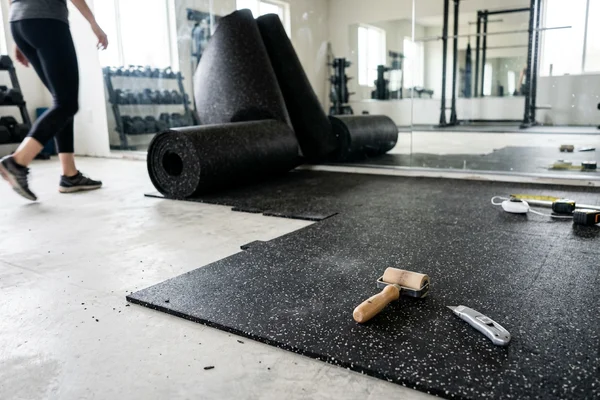 Rolled rubber flooring part unrolled in a fitness studio with tools on the surface