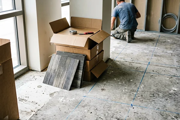 Opened carpet tile cartons on a bare office slab with chalk layout lines