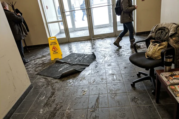 Wet lobby floor with tracked-in slush and a curled loose-laid mat