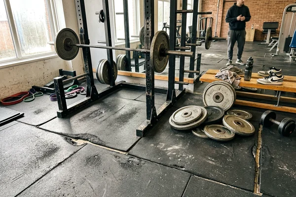 Worn gym flooring with open seams and dents under a weight rack before replacement